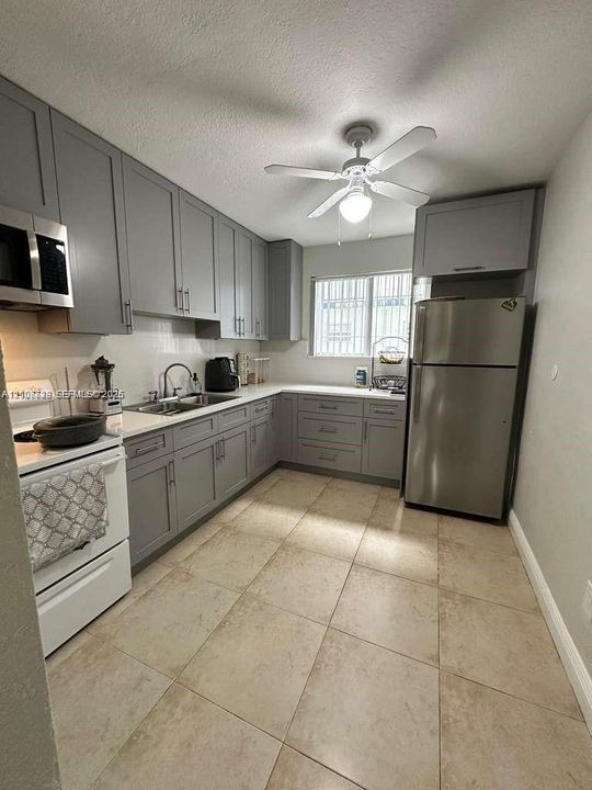 Kitchen featuring grey shaker-style cabinetry, light-toned tile flooring, stainless steel appliances, and quartz countertops
