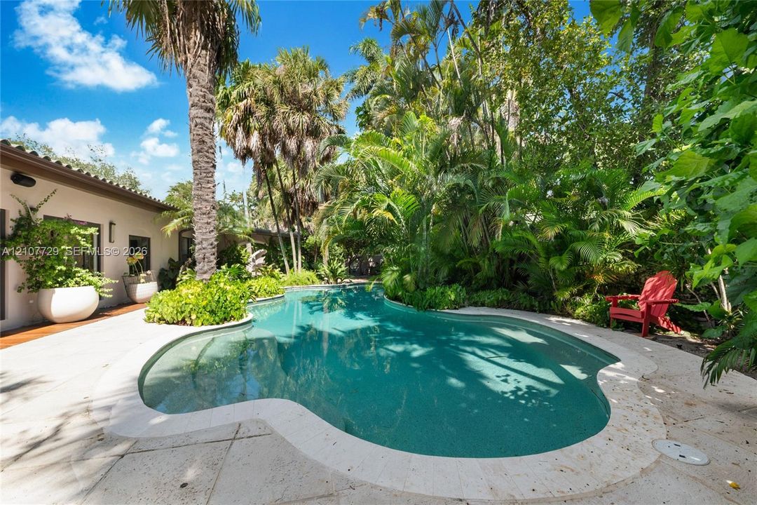 Custom-shaped swimming pool with stone coping, concrete decking, and established tropical landscaping