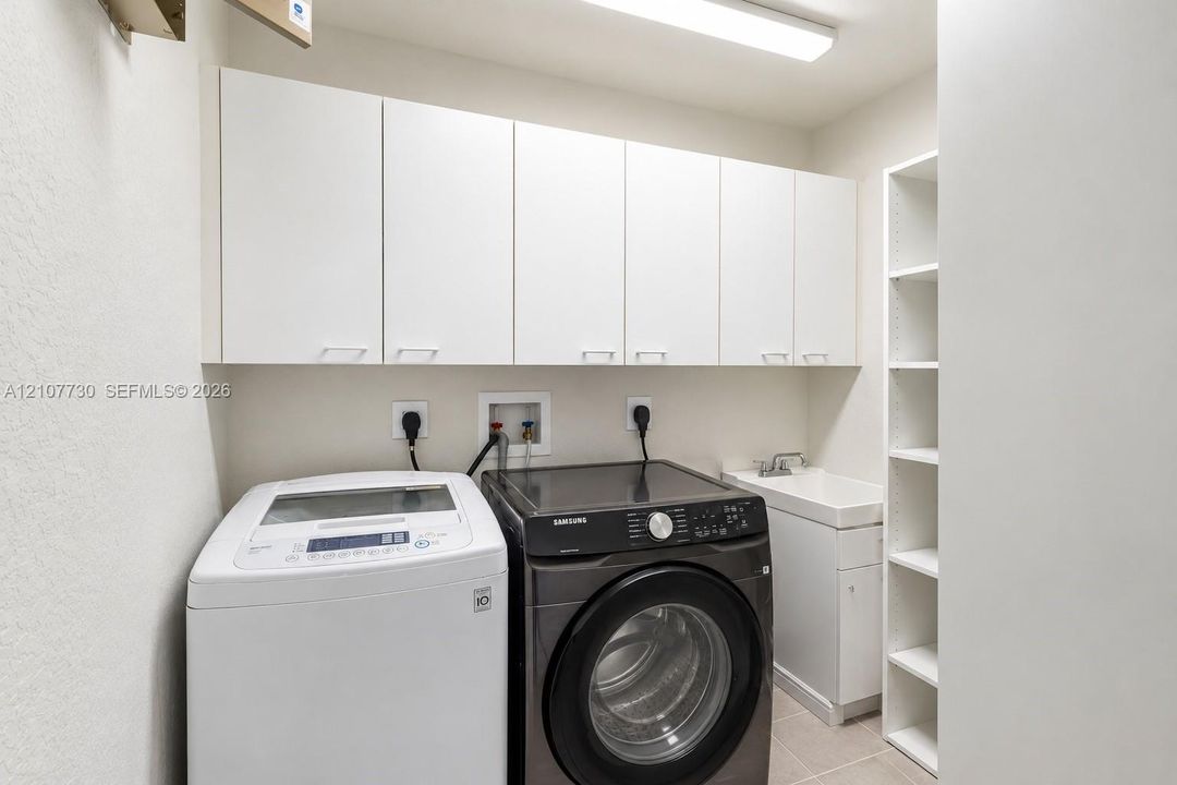 Laundry room featuring white wall-mounted cabinetry, integrated open shelving, a utility sink with white vanity base, and overhead lighting