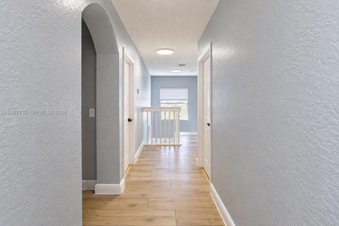 Hallway featuring wood-finish flooring, an arched entryway, white paneled doors, recessed ceiling lighting, and a balustrade staircase railing