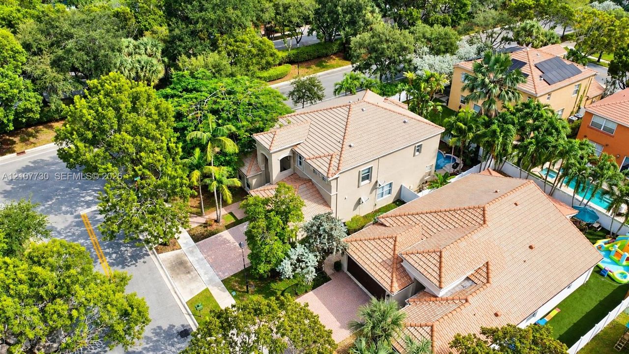 Aerial perspective of a multi-story residence featuring a clay tile roof, paved driveway, integrated garage, and mature landscaping