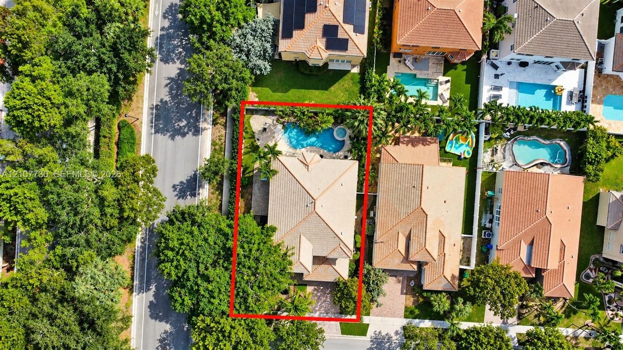 Aerial perspective of a property featuring a tiled roof, an inground swimming pool with a spa, and a paved driveway
