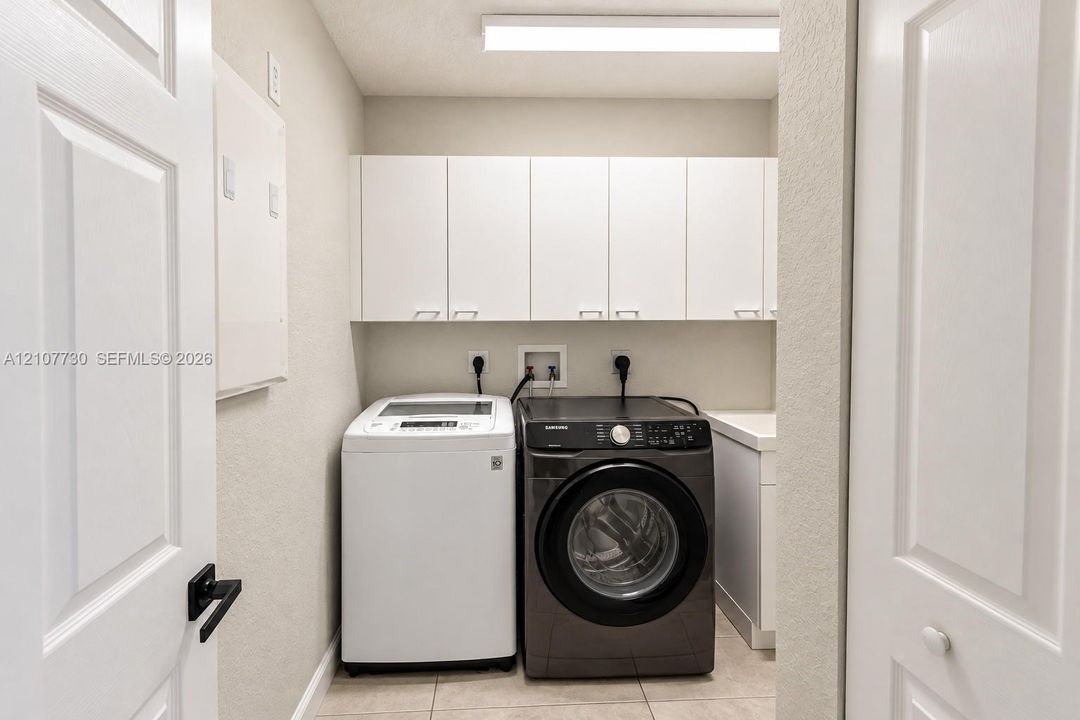 Laundry room featuring white shaker-style wall-mounted cabinetry, tile flooring, and a dedicated utility sink