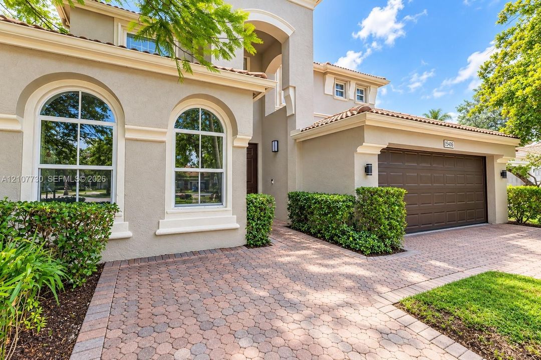 Mediterranean-style exterior featuring a paved stone driveway, arched multi-pane windows, decorative trim accents, a tile roof, and an attached multi-car garage