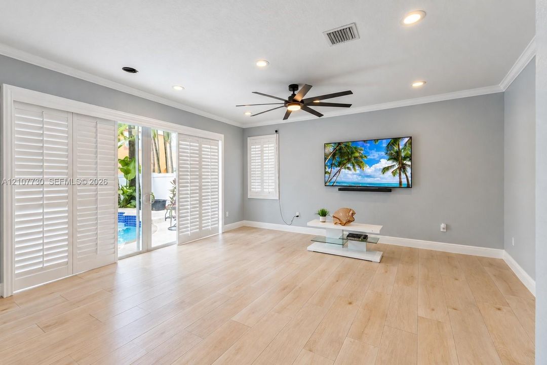 Open-concept room featuring light wood-finish flooring, recessed lighting, a modern ceiling fan, sliding glass doors with plantation shutters, and crown molding