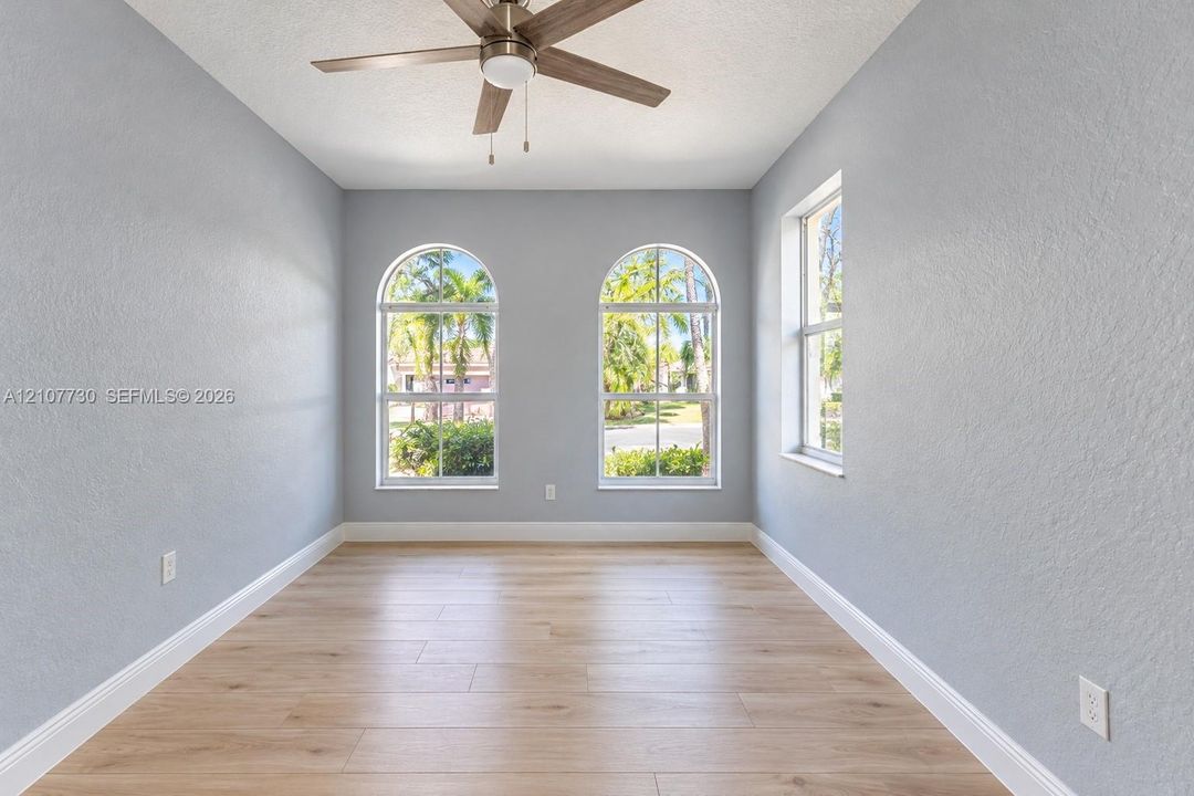 Room featuring wood-finish flooring, two arched windows, a single rectangular window, and a ceiling fan