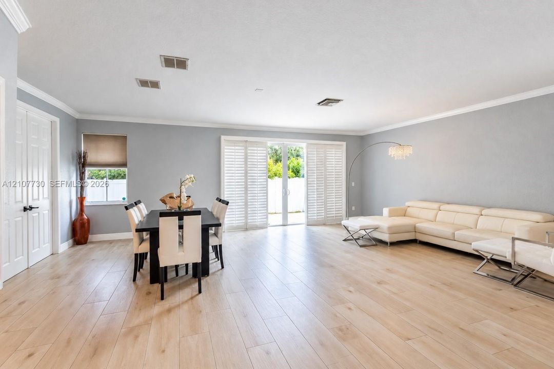 Open-concept floor plan featuring wood-finish flooring, crown molding, sliding glass doors with plantation shutters, and recessed lighting