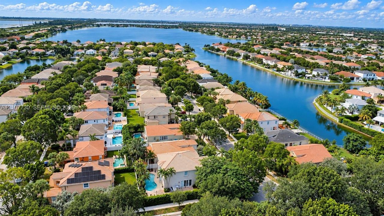Aerial perspective of a residential neighborhood featuring waterfront positioning, tile roof architecture, backyard swimming pools, solar panel installations, and mature landscaping
