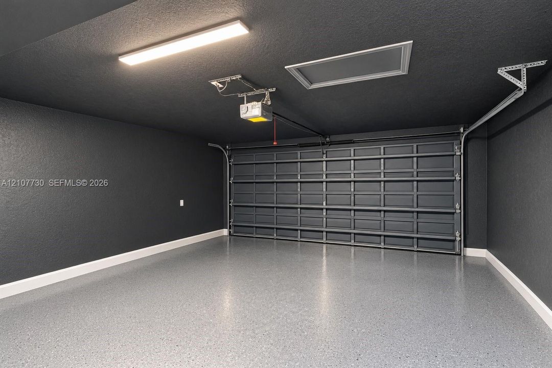 Finished garage space featuring dark-toned walls, a sectional metal garage door, epoxy-coated flooring, and an integrated ceiling light fixture