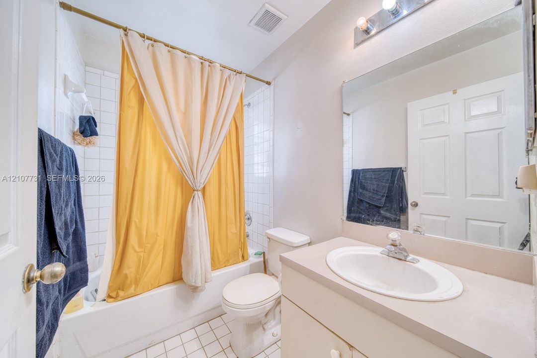 Bathroom featuring a vanity with a white drop-in sink, a wall-to-wall mirror, a combination tub and shower with white tile surround, and tile flooring