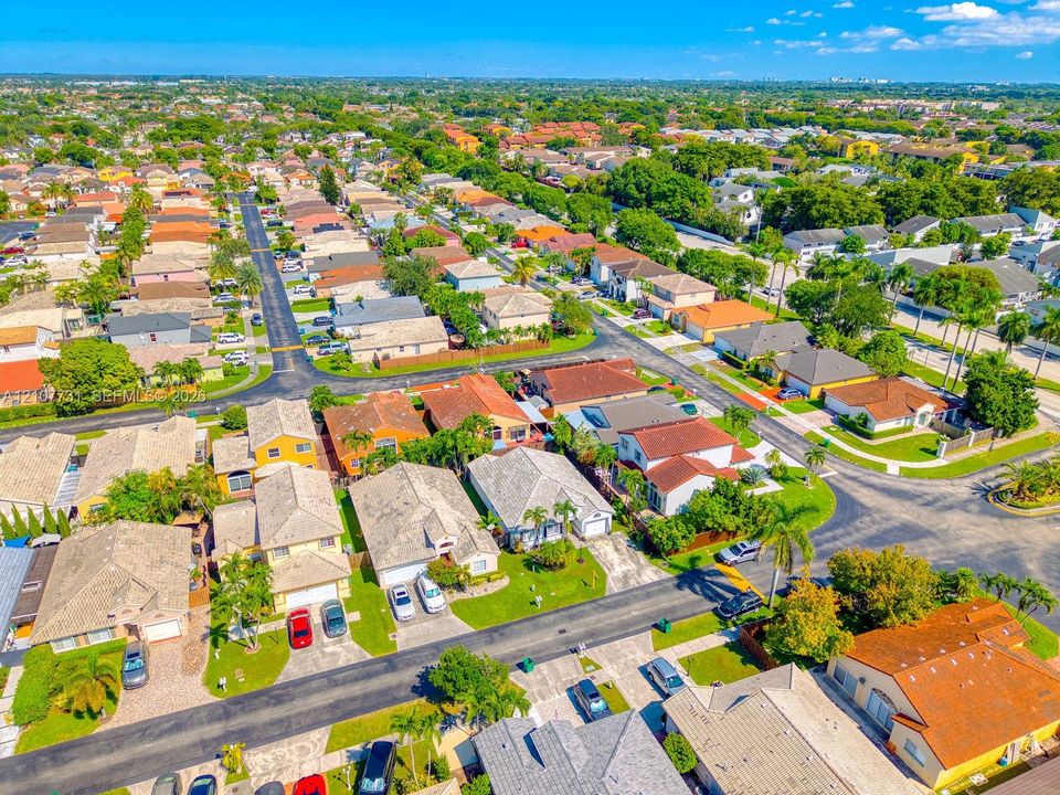 Aerial perspective of a suburban neighborhood featuring paved street grids, detached single-family residences with pitched rooflines, concrete driveways, and established landscaping with palm trees