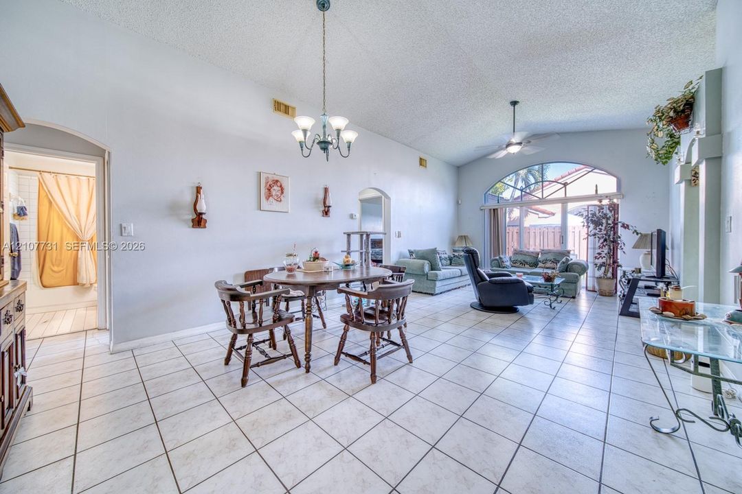 Open-concept living space featuring vaulted ceilings, arched entryways, tile flooring, an arched window, and an integrated hanging light fixture