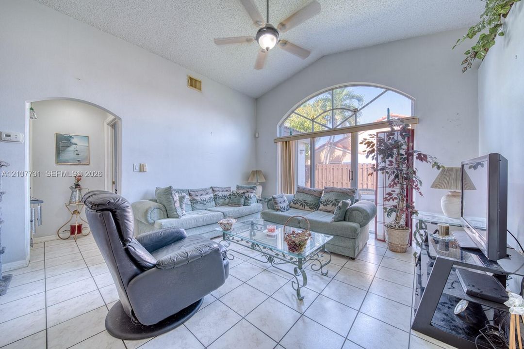 Vaulted ceilings, arched window, sliding glass door, and neutral ceramic tile flooring