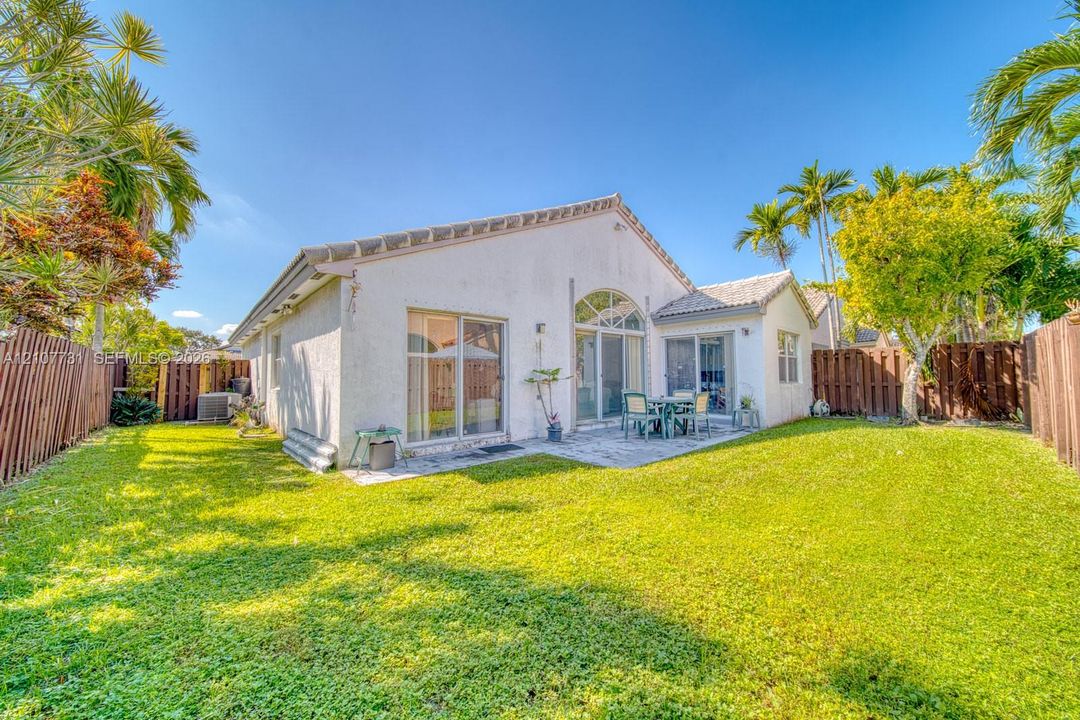 Rear exterior featuring a stucco facade, tiled roof, glass sliding doors, stone patio, and wood privacy fencing