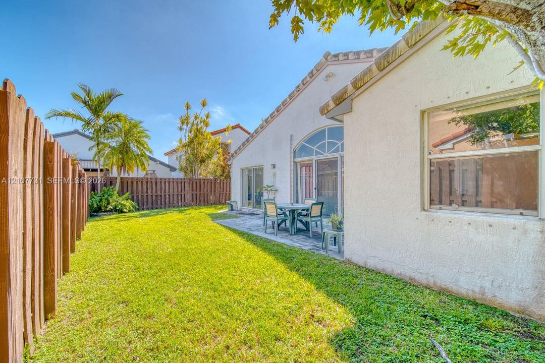 Stucco exterior featuring a paved rear patio, arched window detailing, and a privacy wood-slat fence enclosing the backyard