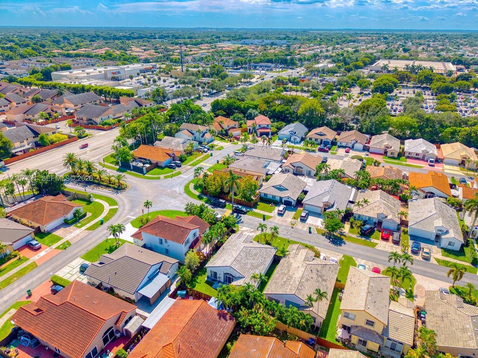 Aerial perspective of a suburban neighborhood featuring residential homes with tile roofing, paved streets, and mature landscaping