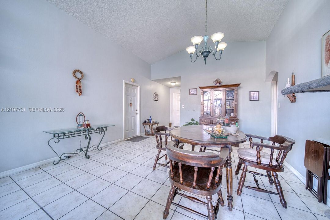 Vaulted ceilings, neutral wall tones, ceramic tile flooring, and decorative multi-arm chandelier lighting