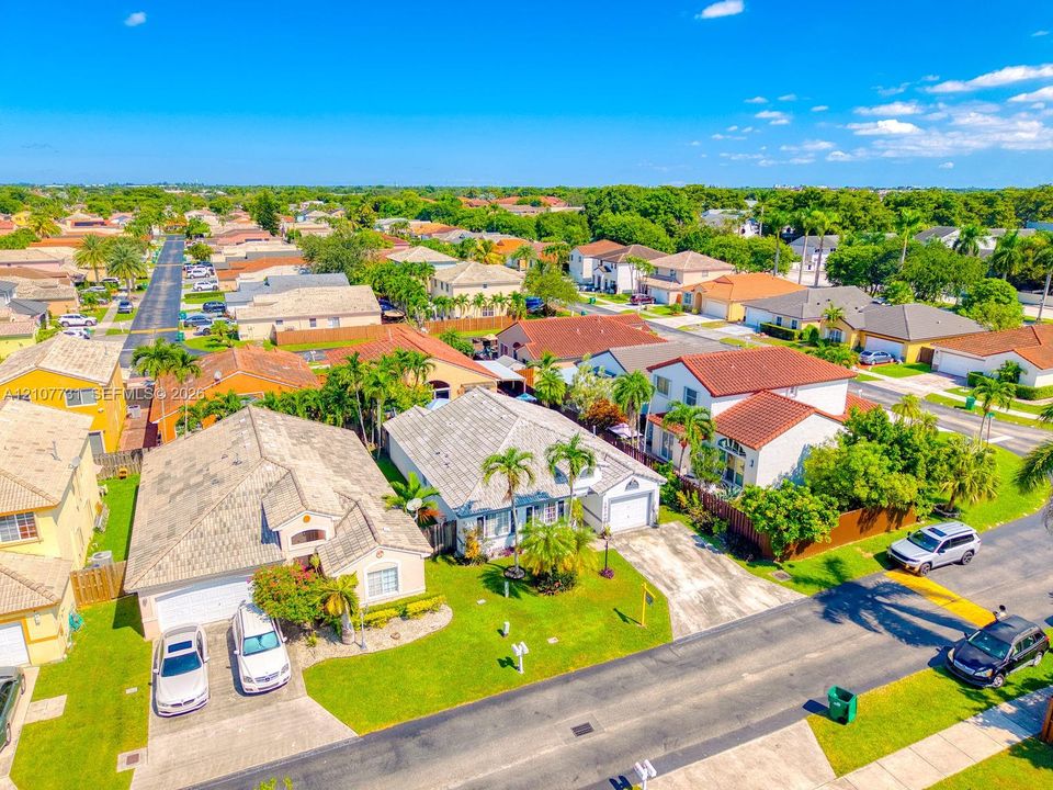 Aerial perspective of a residential neighborhood featuring tiled rooflines, manicured lawns, mature palm trees, paved driveways, and concrete streetscapes