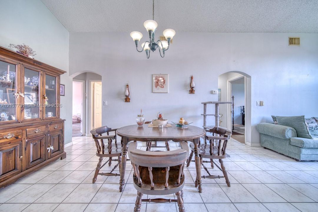 Dining area featuring vaulted ceilings, ceramic tile flooring, arched doorways, and an overhead multi-light chandelier