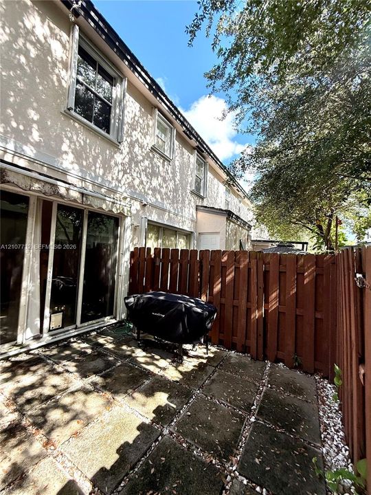 Private patio featuring stone pavers, enclosed by a wood privacy fence, with sliding glass door access