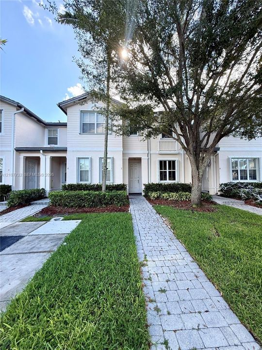 Two-story exterior featuring lap siding, multi-pane windows, a paved walkway, manicured hedging, and mature landscaping