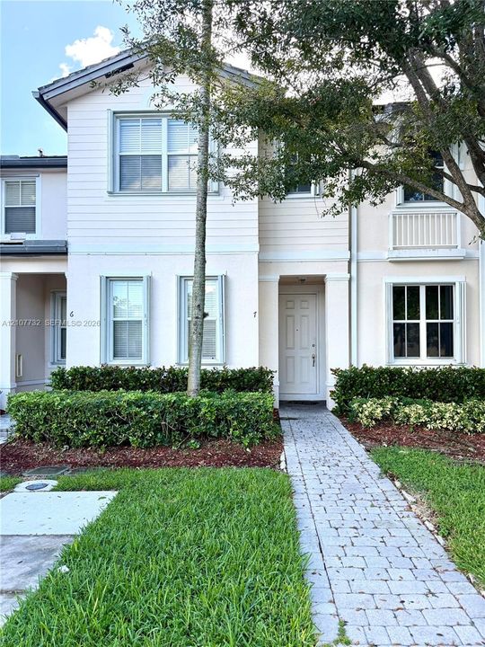 Two-story townhome exterior featuring horizontal lap siding, a paved stone walkway, multi-pane windows, and a built-in upper-level balcony with railings