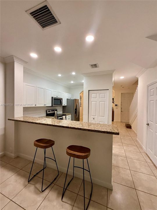 Kitchen featuring a stone-look countertop breakfast bar, white cabinetry, recessed lighting, and tile flooring