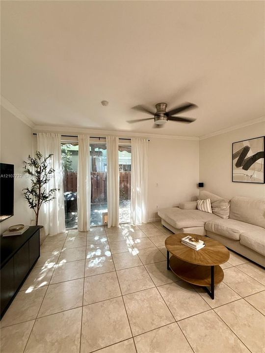 Large-format neutral floor tile, ceiling fan, and sliding glass door with external patio access