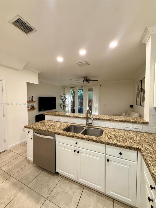 Kitchen featuring white cabinetry, stone-surface countertops, dual-basin stainless steel sink, recessed lighting, and tile flooring
