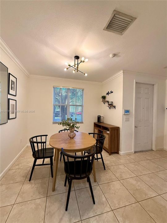 Neutral-toned interior featuring ceramic tile flooring, crown molding, multi-arm geometric ceiling lighting, and a window with horizontal blinds