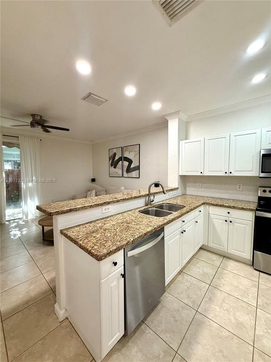 Kitchen featuring white cabinetry, stone-surface countertops, stainless steel appliances, dual-basin sink, and ceramic tile flooring