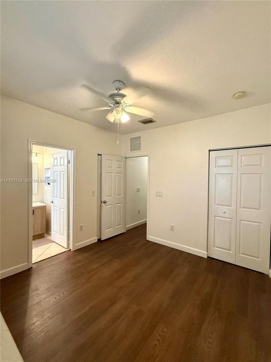 Interior space featuring wood-finish flooring, white paneled doors, ceiling fan with integrated lighting, and dual-door closet storage