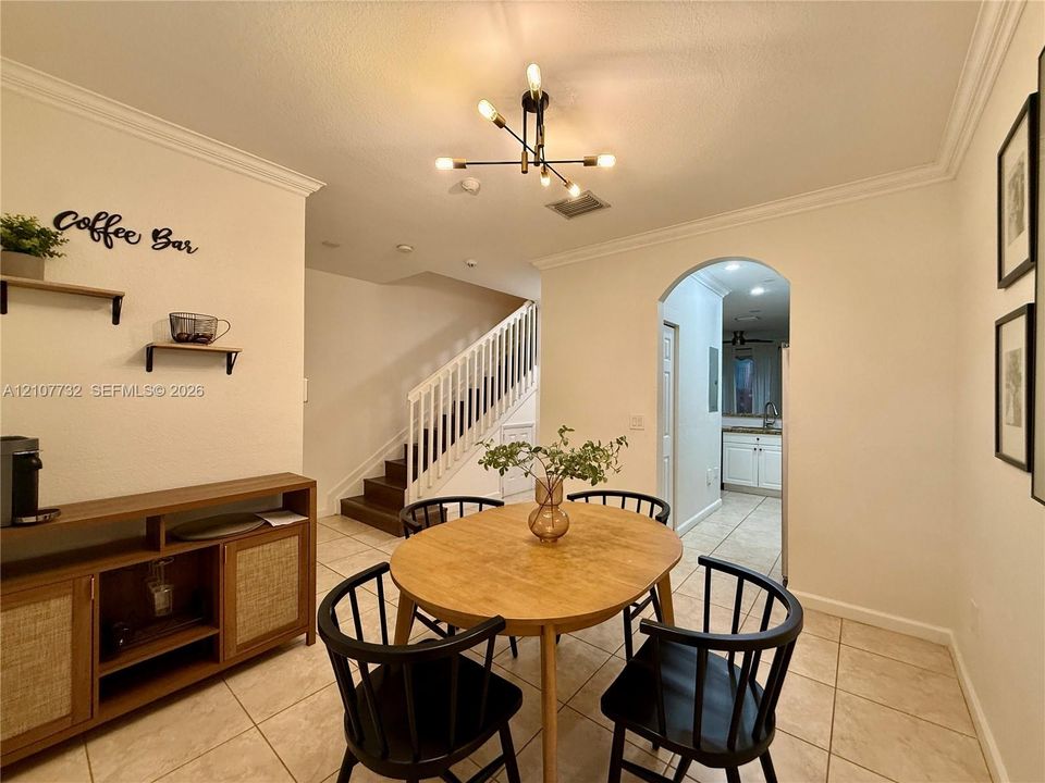 Dining area featuring ceramic tile flooring, crown molding, a multi-arm modern light fixture, and an arched entryway leading to the kitchen