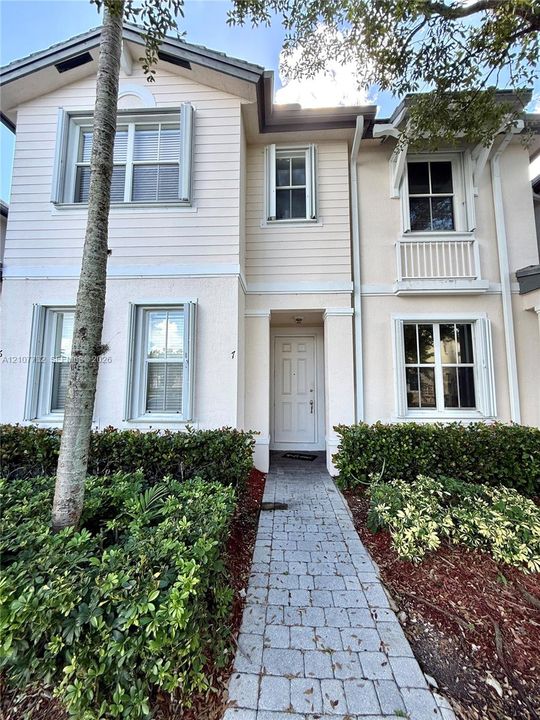 Two-story exterior featuring a mix of horizontal lap siding and textured stucco, accented by a decorative balcony, multi-pane windows with louvered shutters, and a stone-paver walkway