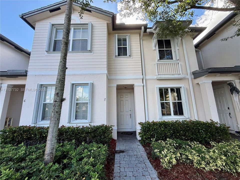Two-story exterior featuring a mix of horizontal lap siding and textured stucco finish, a covered entryway, decorative upper-level balcony railing, and a stone-paver walkway