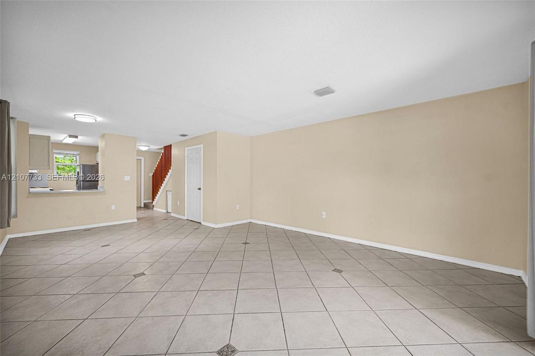 Open-concept interior featuring large-format diagonal tile flooring with decorative inlay accents, neutral wall tones, recessed ceiling lighting, and a built-in staircase with a wood-finish handrail