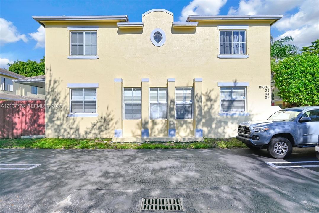 Two-story exterior featuring a stucco finish, rhythmic vertical columns, an arched roofline parapet, a central oval window, and grid-patterned windows