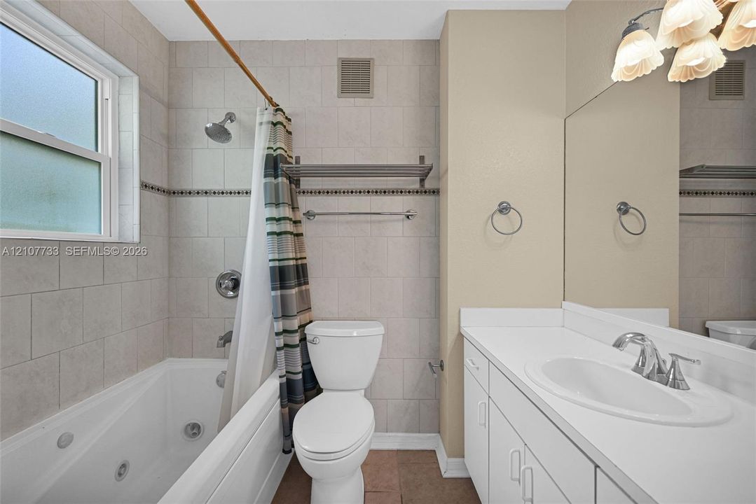 Bathroom featuring a jetted soaking tub with a tiled surround, a white vanity with an integrated basin, a large wall-mounted mirror, and decorative wall lighting
