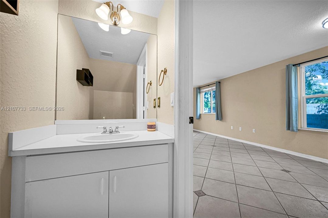 Bathroom vanity featuring a white cabinet, solid-surface countertop with an integrated oval sink, and a large-format mirror with multi-bulb overhead lighting, complemented by tile flooring with decorative inserts