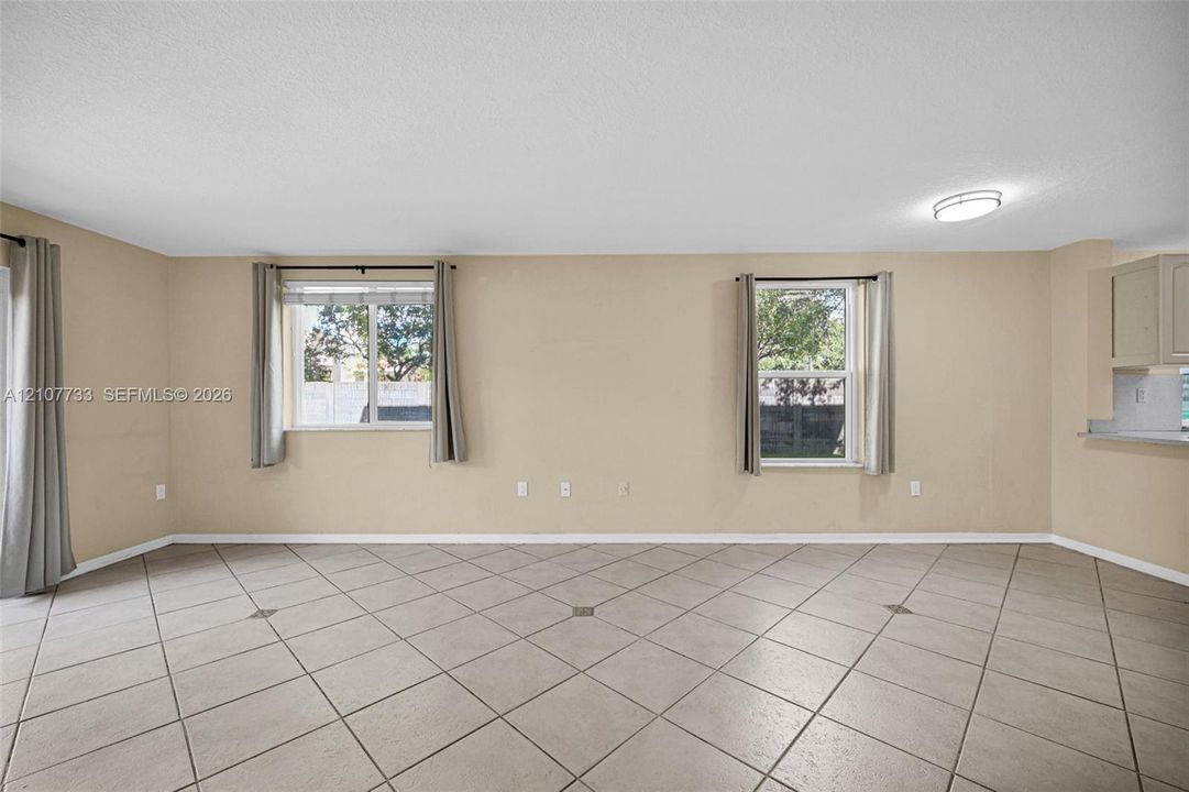 Spacious room featuring neutral wall tones, large-format tile flooring, dual windows, and recessed ceiling lighting