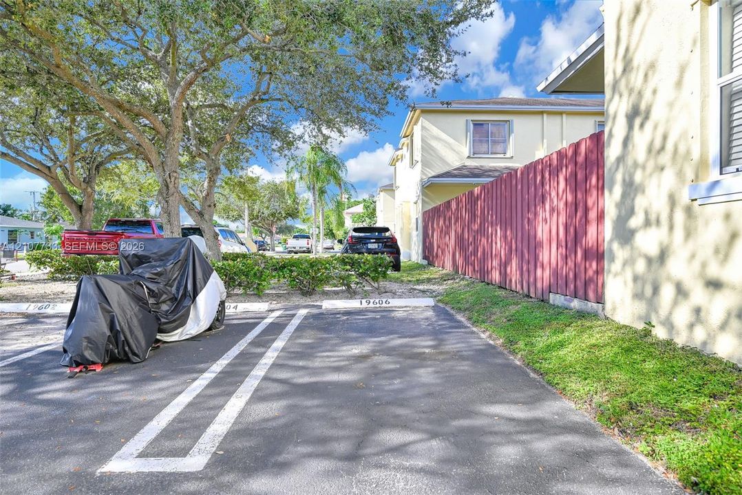 Asphalt-paved parking area featuring designated spaces, stucco exterior walls, and privacy fencing