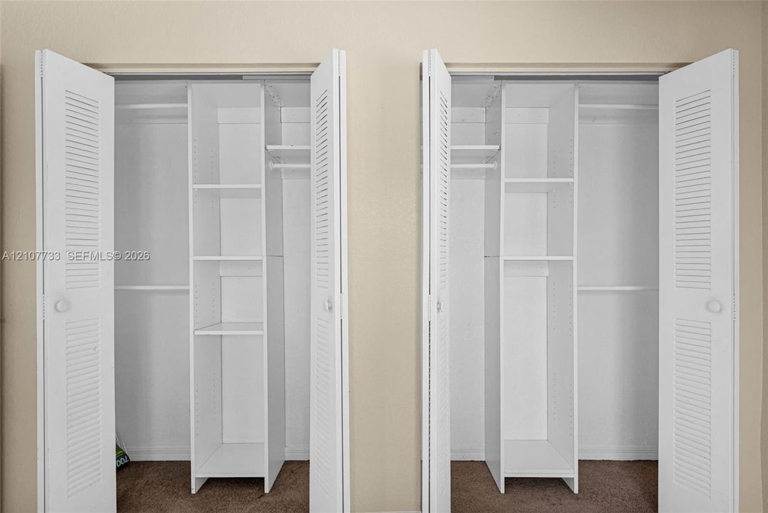 Dual closets featuring white louvered doors, built-in shelving towers, and integrated hanging rods