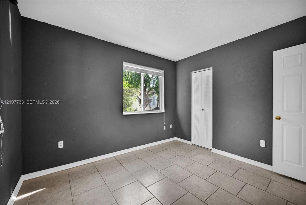 Room featuring tile flooring, neutral painted walls, a sliding louvered closet door, and a single-pane window