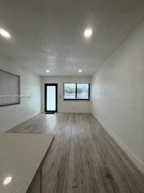 Interior space featuring wood-finish flooring, recessed lighting, white walls, a single-lite exterior door with a dark frame, and a stone-surface peninsula