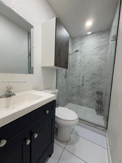 Bathroom featuring a dark-finish vanity with a white integrated sink, walk-in shower with glass enclosure, large-format wall tile, and hexagonal floor tile