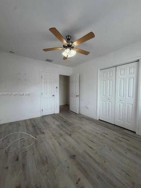 Room featuring wood-finish flooring, a five-blade ceiling fan with integrated lighting, and multi-panel interior doors, including a double-door closet
