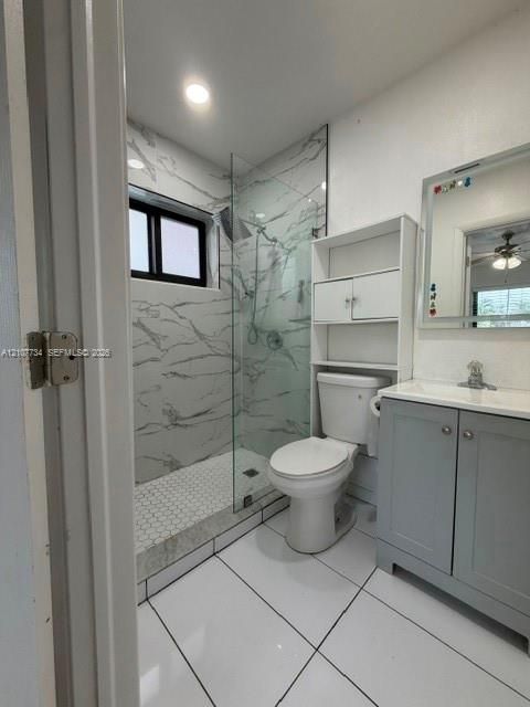 Walk-in shower with stone-finish wall tile, hexagon floor tile, glass enclosure, grey cabinetry, and white tile flooring