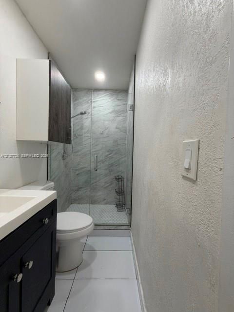 Bathroom featuring a dark-finish vanity with a rectangular sink, wall-mounted storage cabinet, large-format tile flooring, and a walk-in shower with stone-patterned wall tile and a glass door