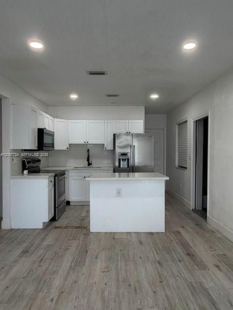 Kitchen featuring white shaker-style cabinetry, wood-finish flooring, recessed lighting, stainless steel appliances, and a central island with a stone-surface countertop