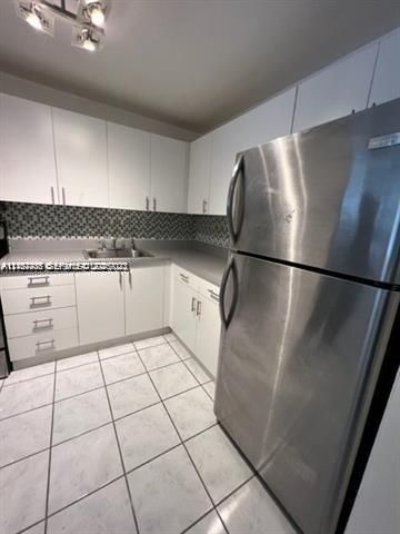 Kitchen featuring white cabinetry, stainless steel refrigerator, patterned tile backsplash, solid-surface countertops, and tiled flooring